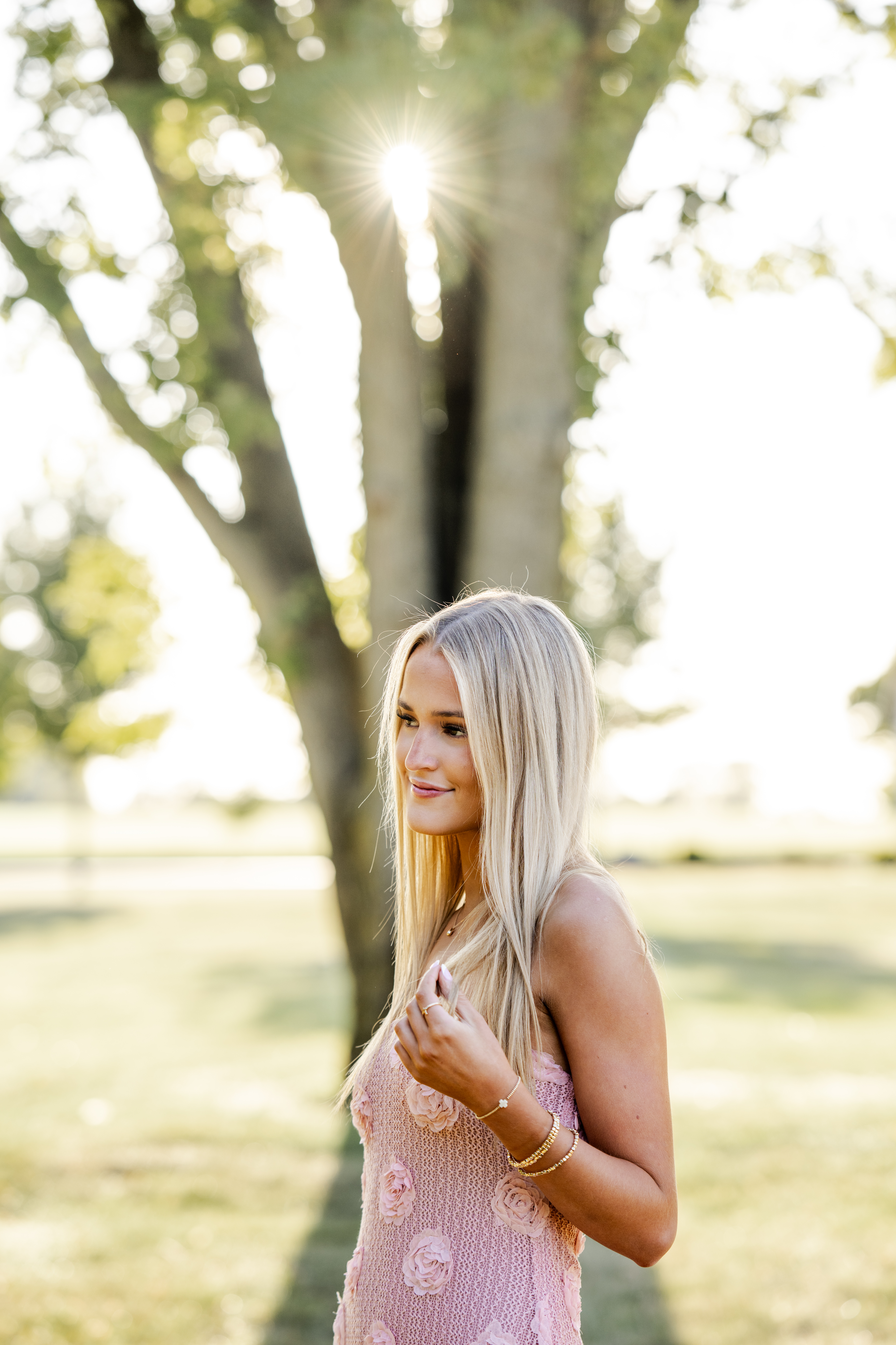 Teen girl plays with her hair and smiles during senior session in golden evening light.