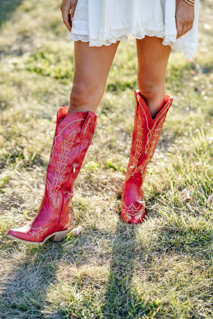 Close-up of red cowboy boots in the grass during golden hour senior photo session.