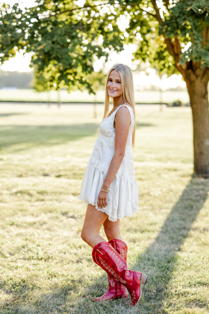 Teen girl poses in red cowboy boots during golden hour senior portraits by Kate Kosnoff