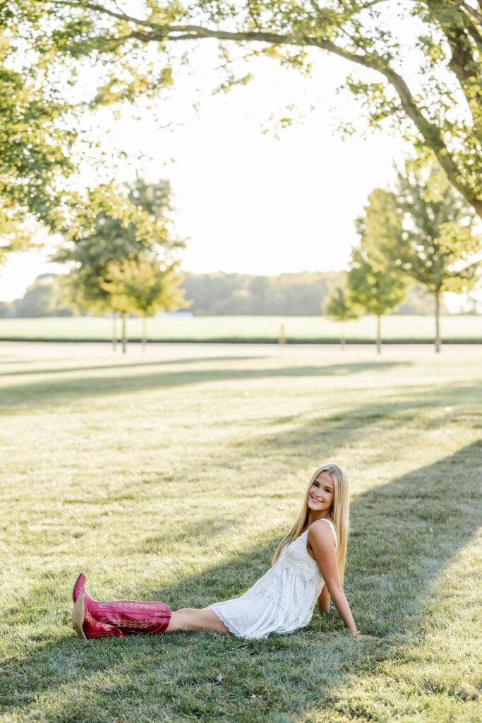 Senior girl reclines in the grass surrounded by soft golden light during equestrian photo session.