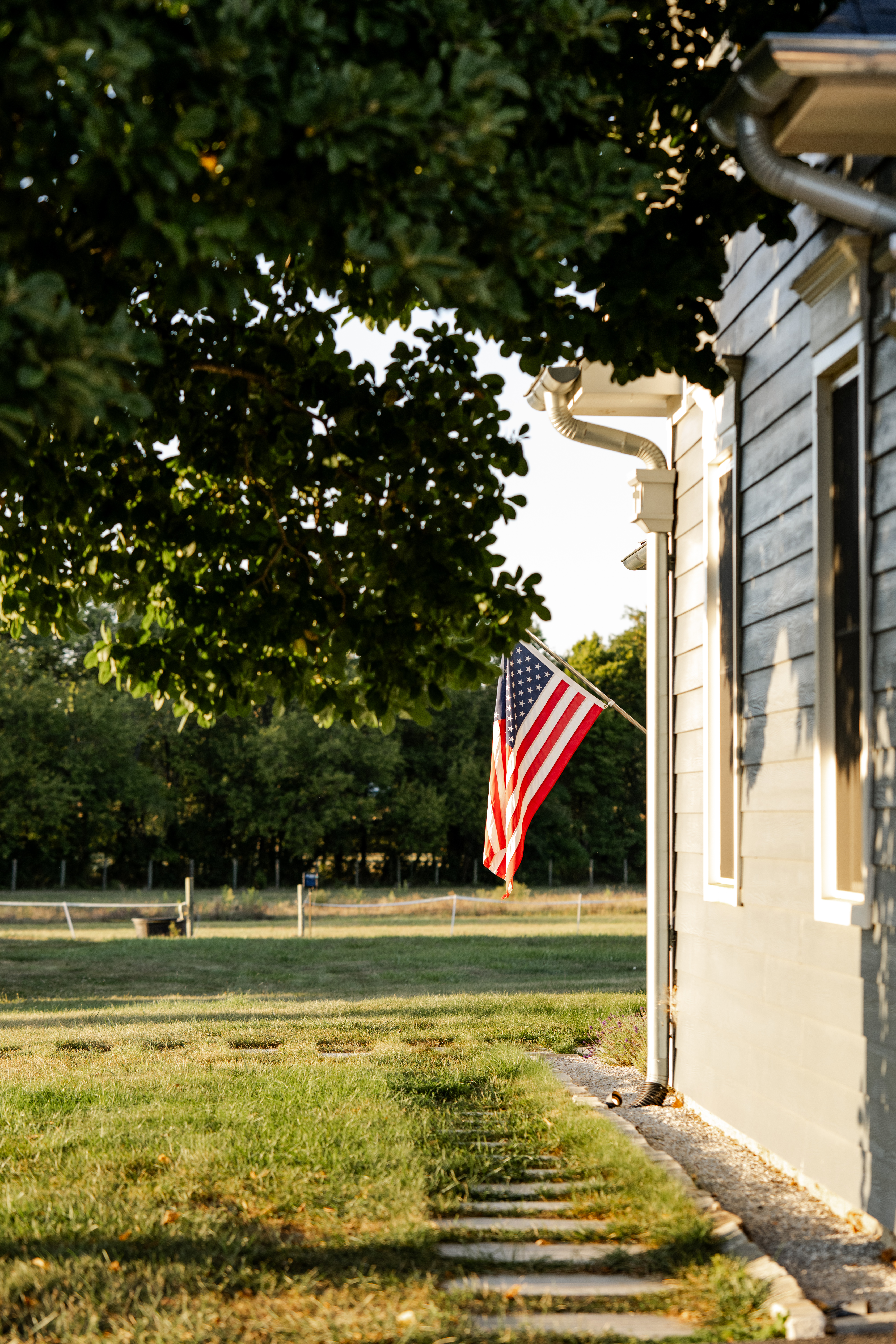 American flag on farmhouse glows in late-day sunlight during senior photo session in Sheridan, Indiana.