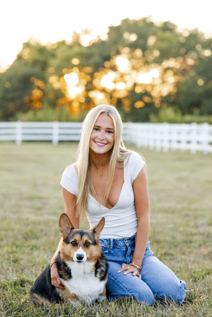 Senior girl cuddles her corgi in warm sunset light during golden hour equestrian photos.